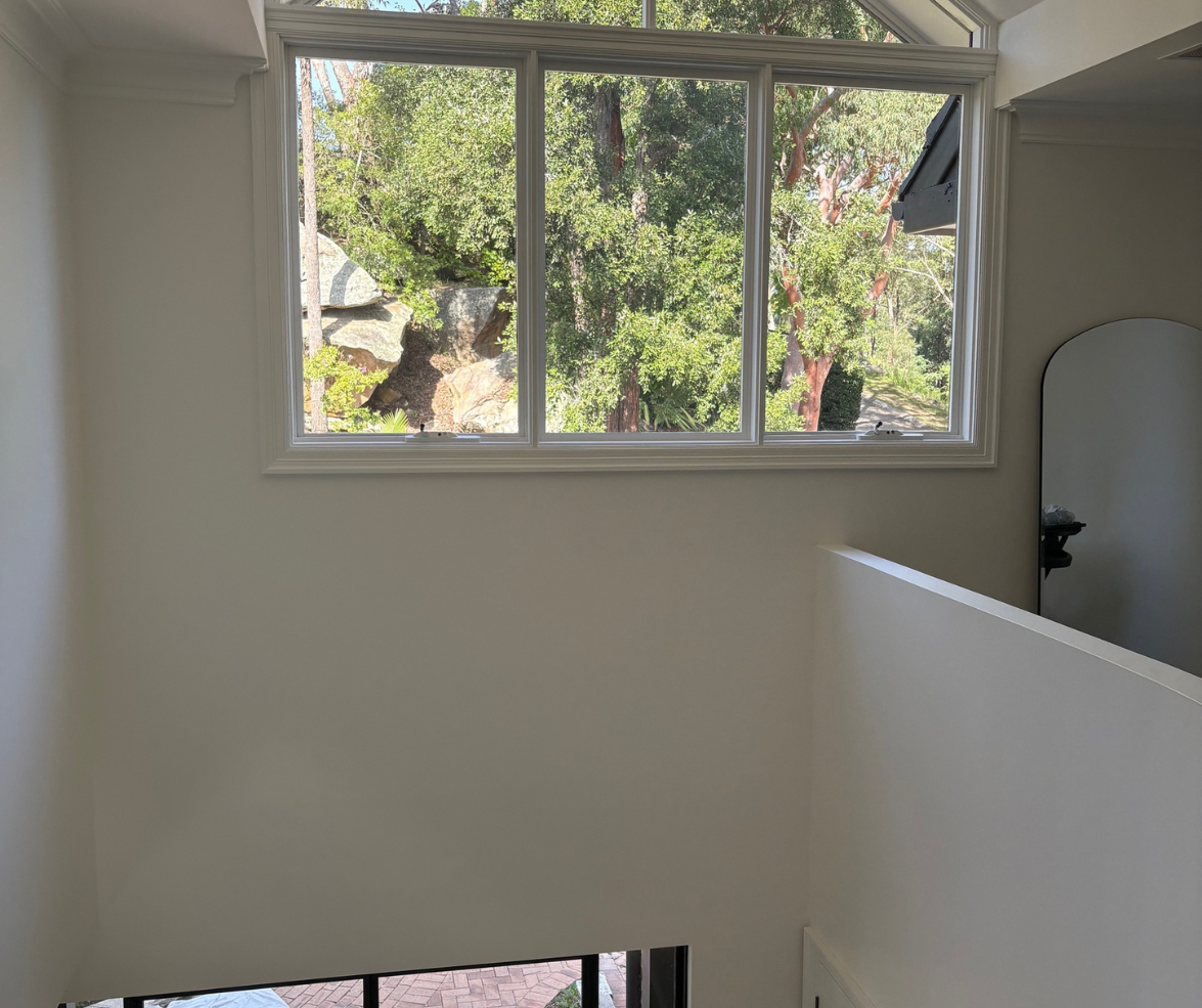 Bright interior with a large window overlooking trees and a white stair railing below. Bright interior with a large window overlooking trees and a white stair railing below.
