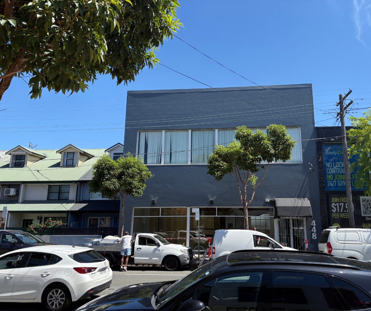 Modern gray storefront on a sunny street with parked cars and trees in front Modern gray storefront on a sunny street with parked cars and trees in front