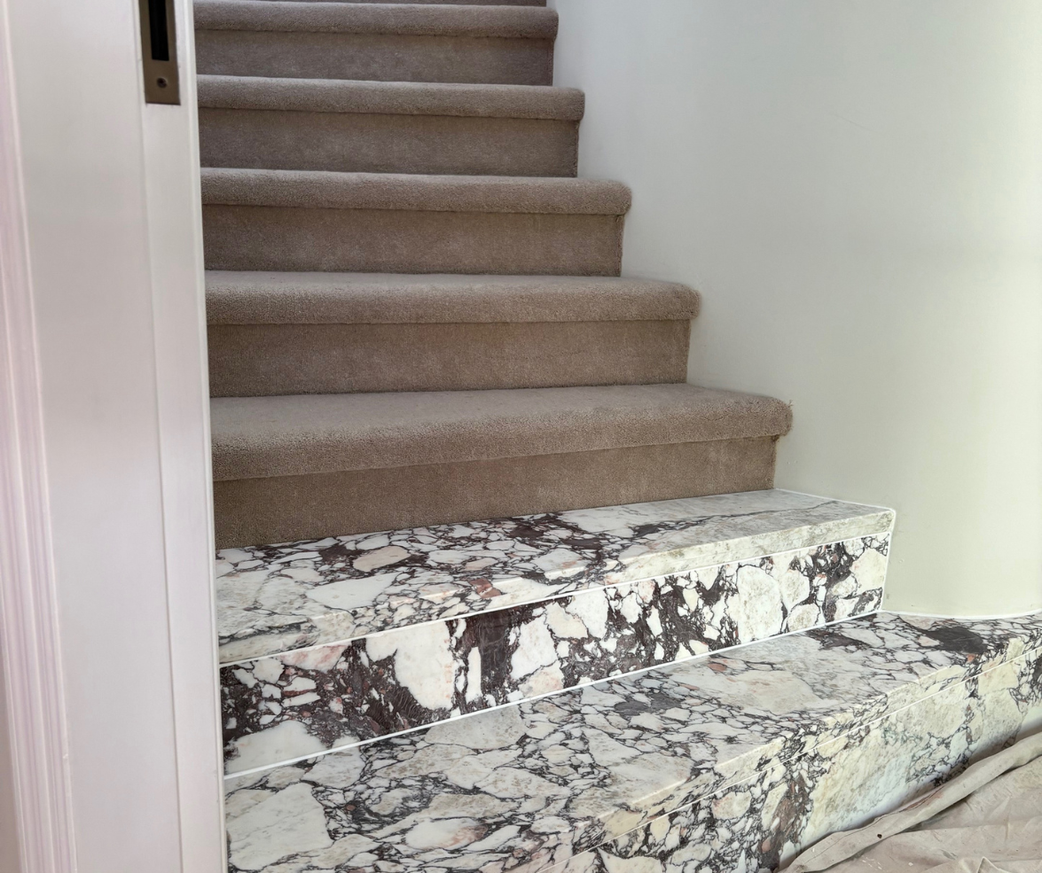 Carpeted staircase with a marble-patterned step at the bottom in a home interior Carpeted staircase with a marble-patterned step at the bottom in a home interior