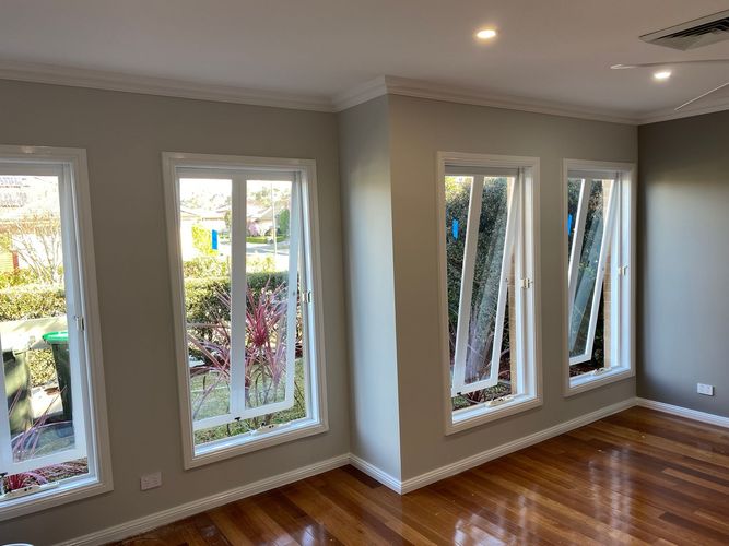An interior room with hardwood floors, neutral-colored walls, and four large windows showing an outdoor garden.