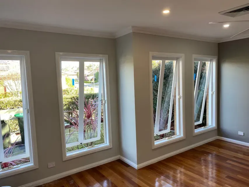 An interior room with hardwood floors, neutral-colored walls, and four large windows showing an outdoor garden.
