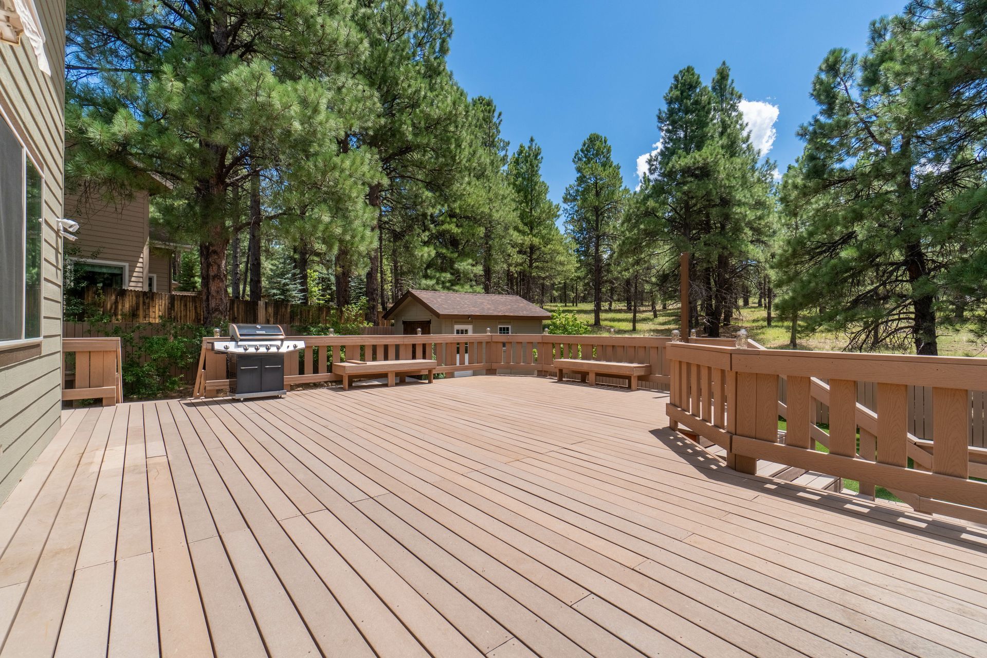 A large wooden deck with a grill and trees in the background.