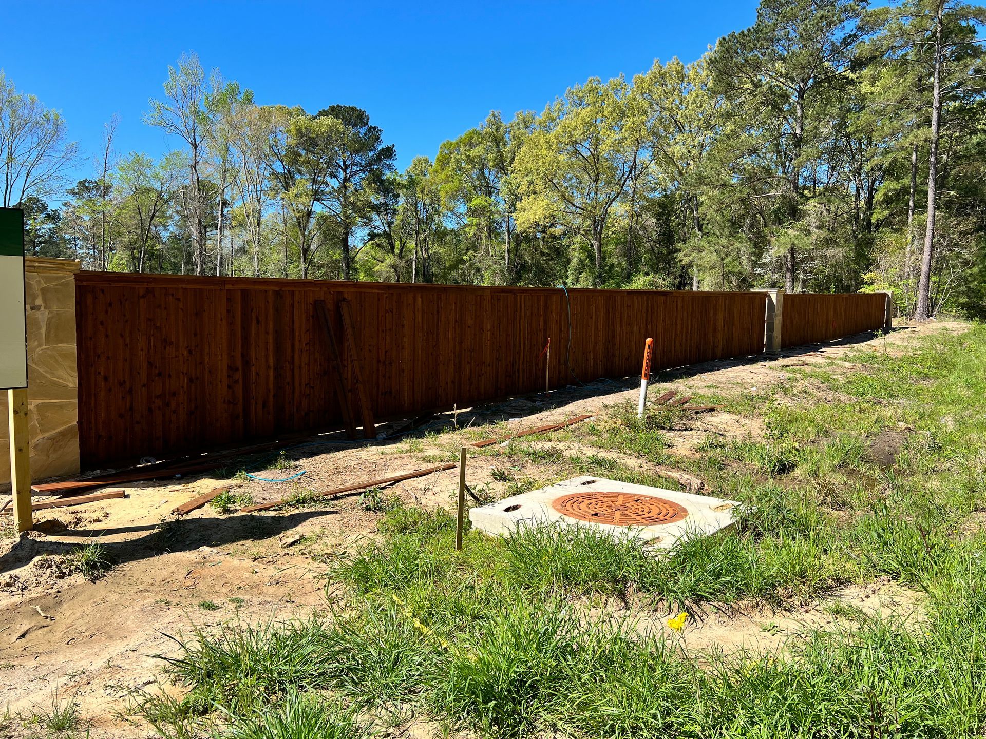 A wooden fence surrounds a grassy field with trees in the background.