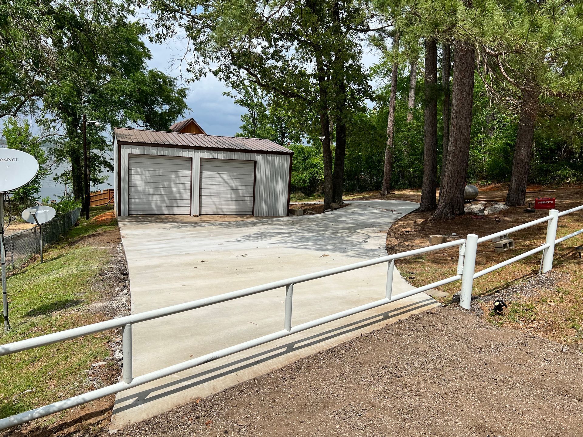 A concrete driveway leading to a garage with a white fence.