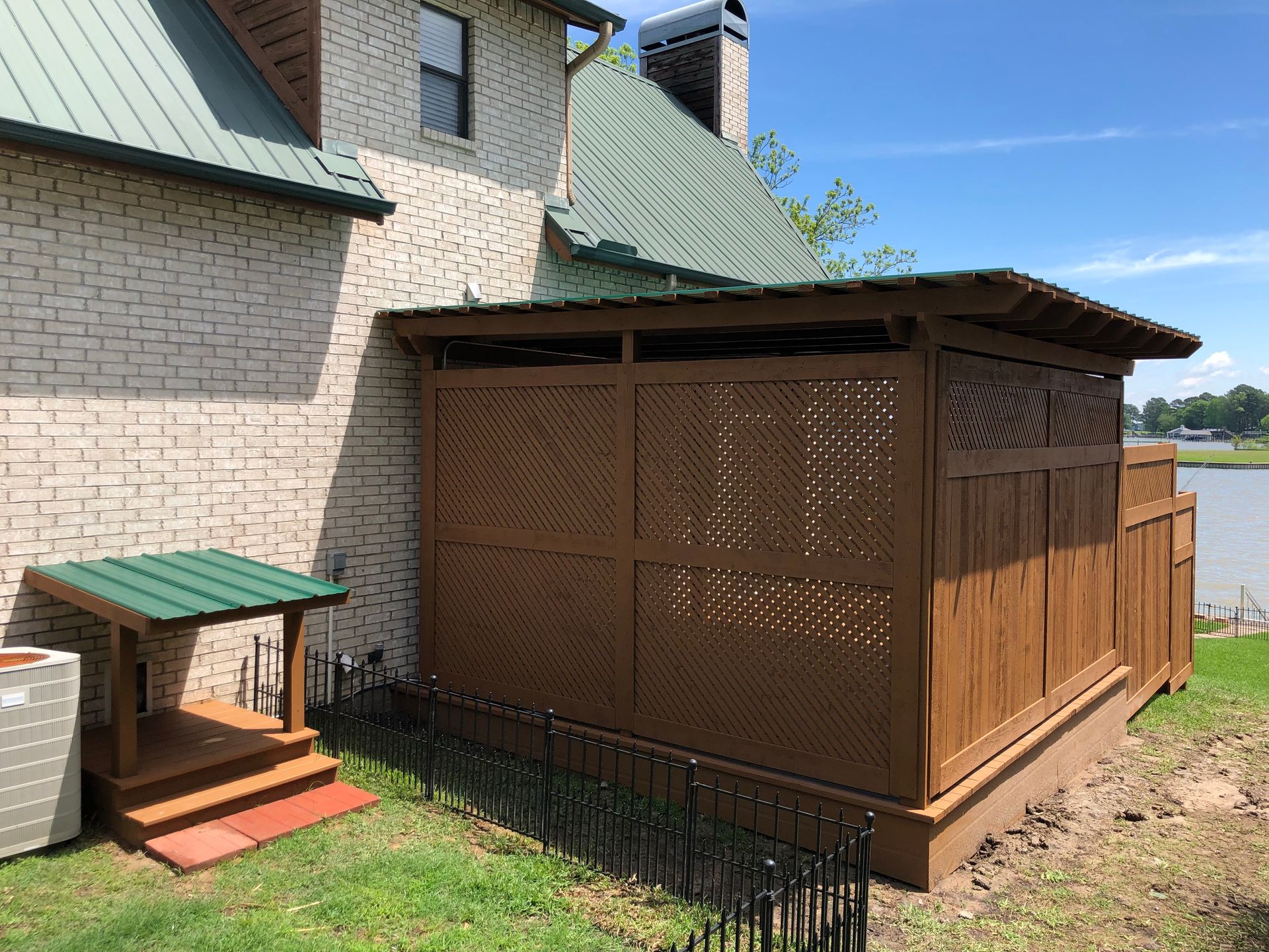 A wooden shed with a green roof is in the backyard of a house.