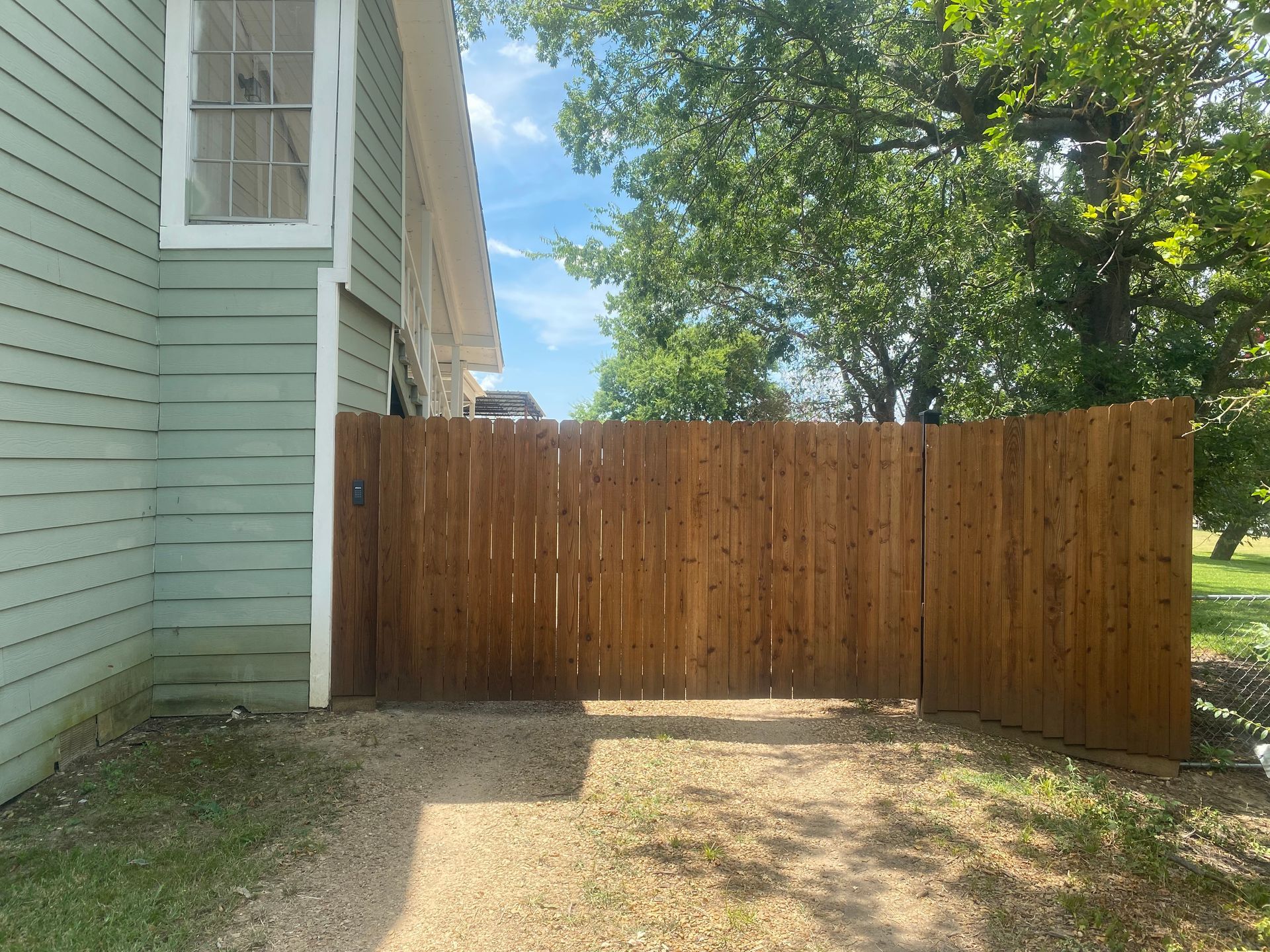 A wooden fence surrounds a driveway leading to a house.