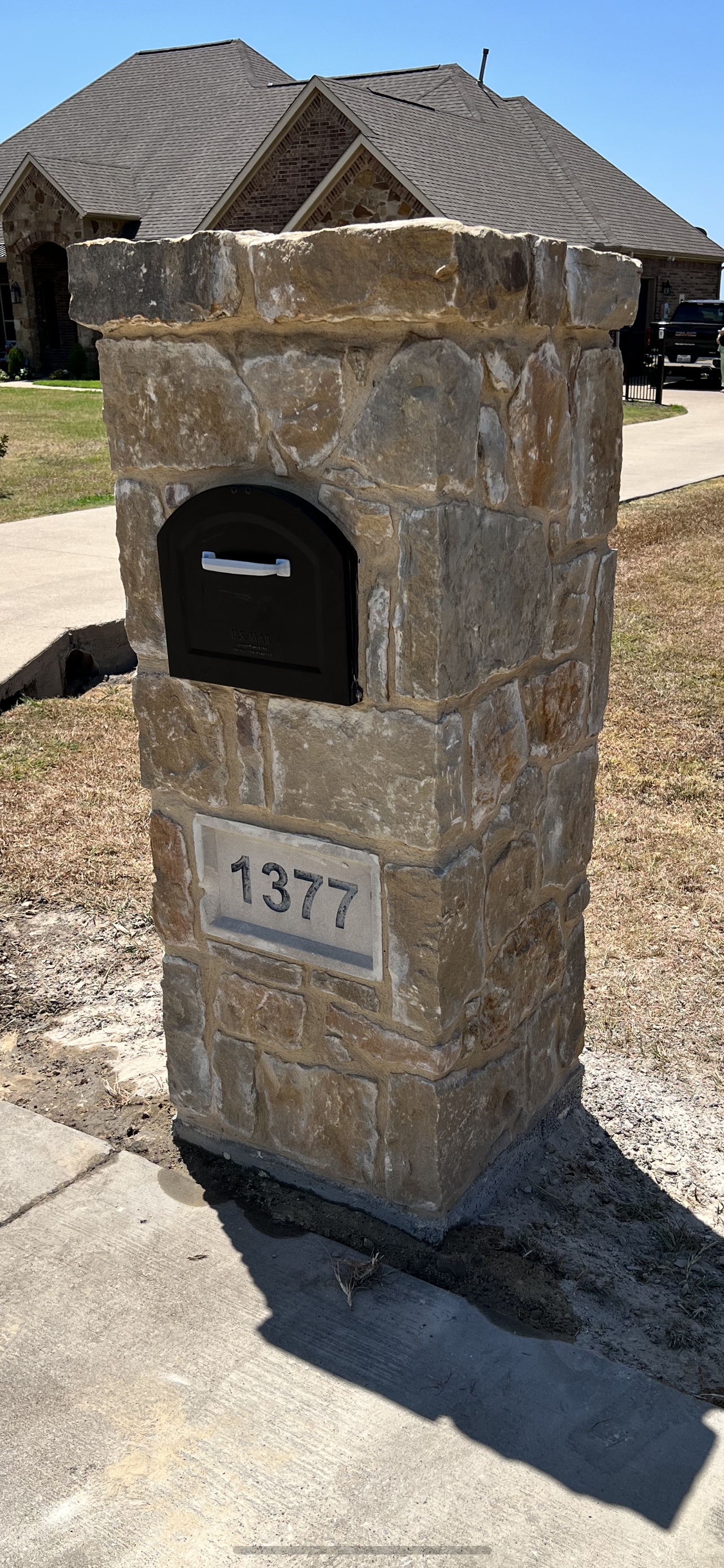 A mailbox is sitting on top of a stone pillar in front of a house.