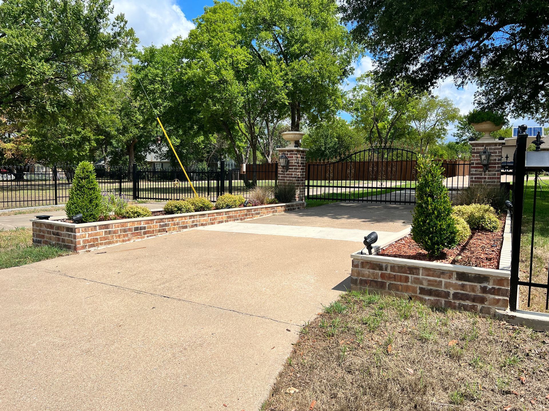 A driveway with brick planters and trees in the background