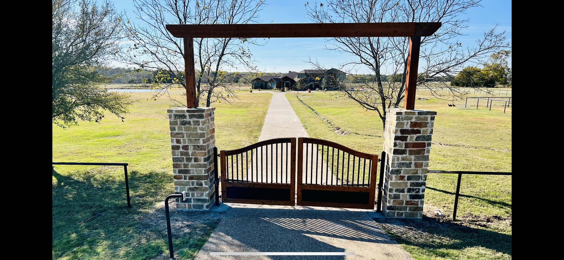 A wooden gate is leading to a dirt road in a field.