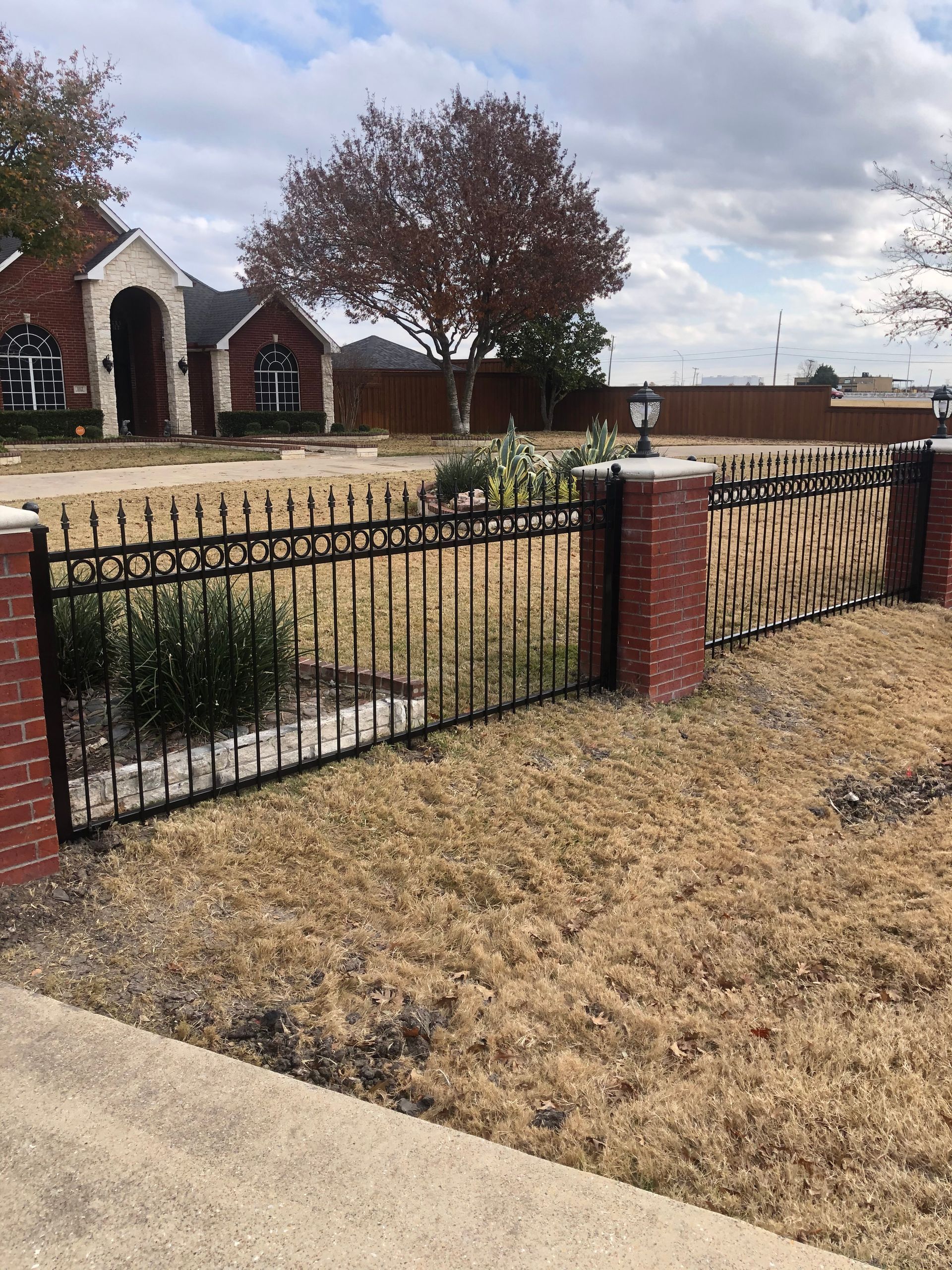 A metal fence surrounds a brick wall in front of a house.