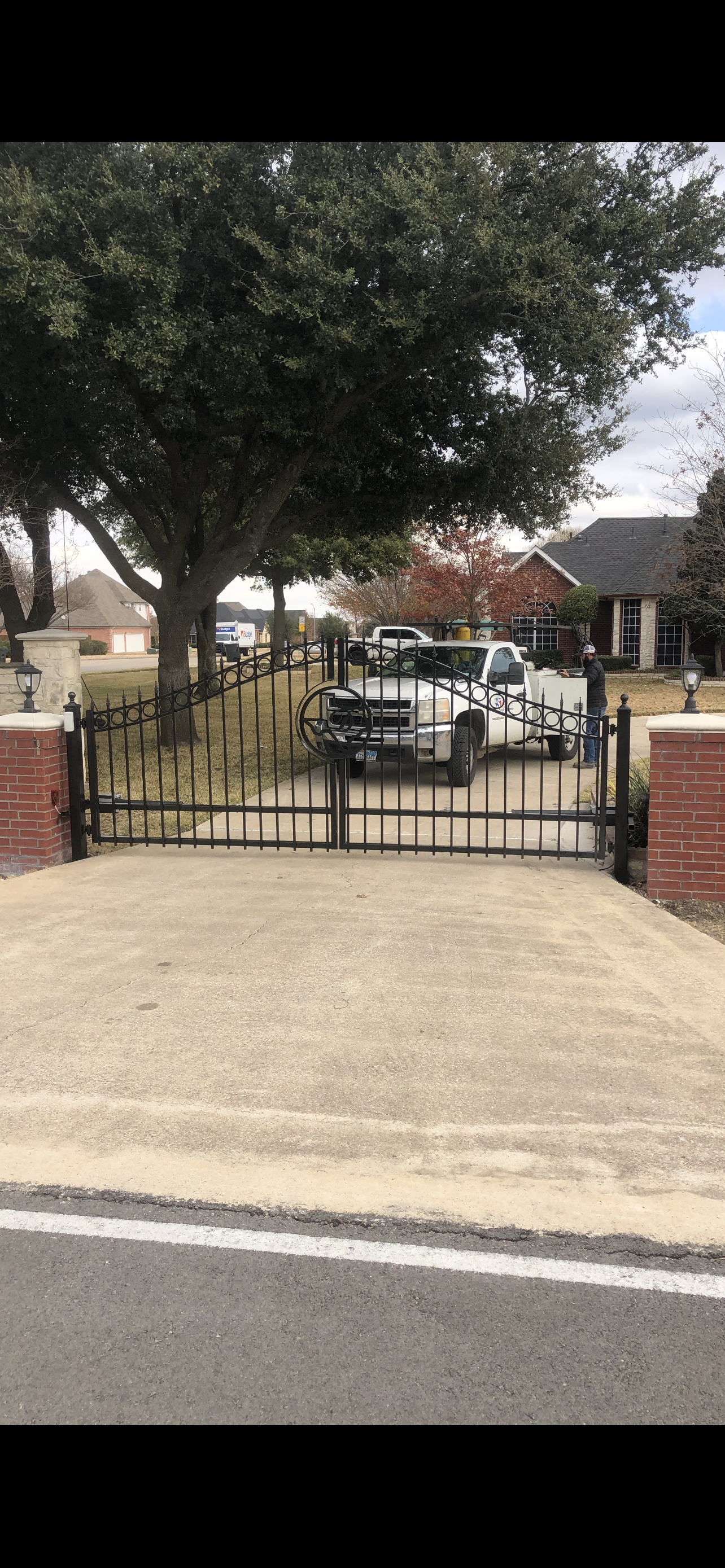 A black wrought iron gate is sitting in the middle of a driveway next to a road.