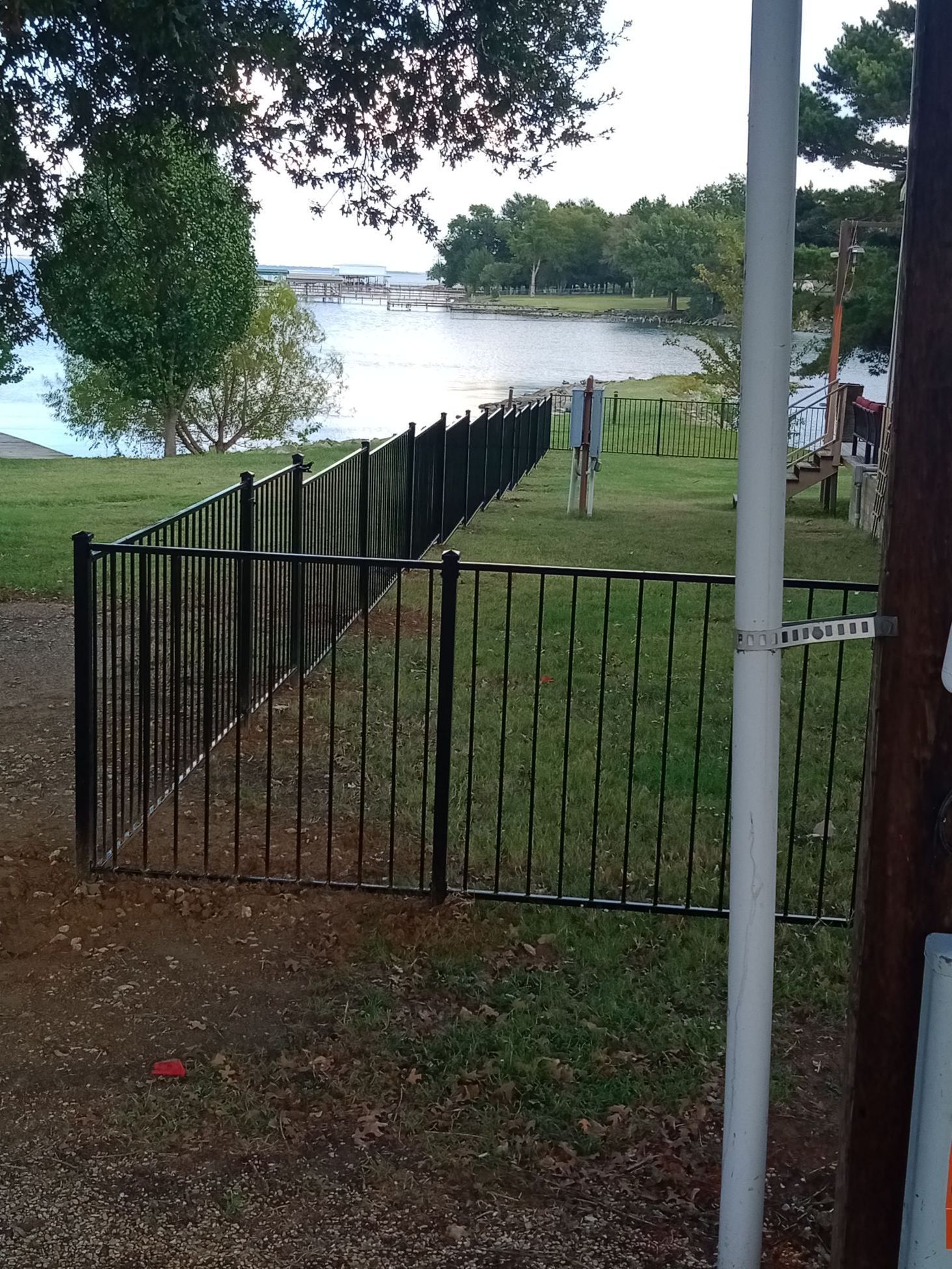 A wrought iron fence surrounds a grassy area with a lake in the background