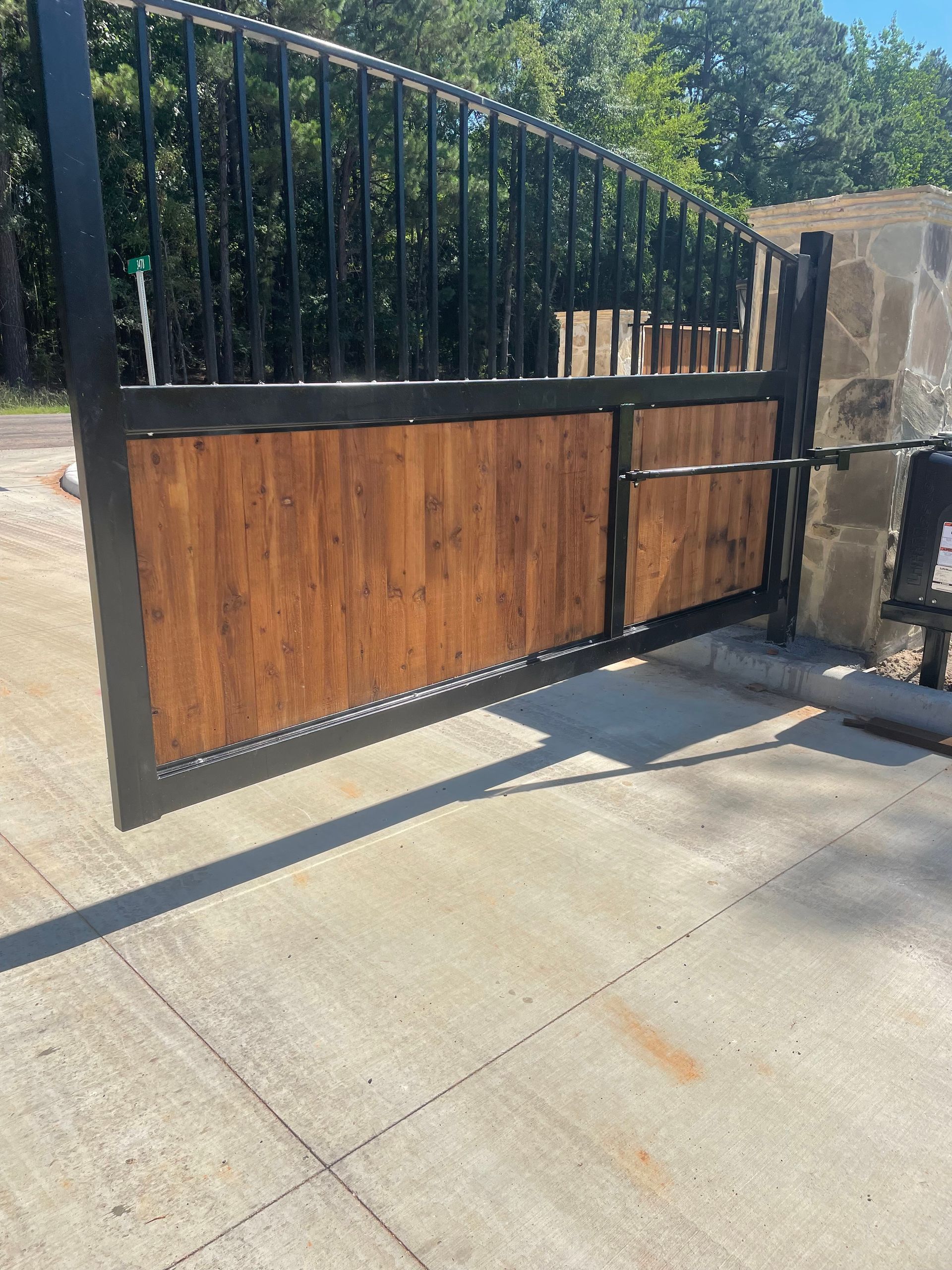 A wooden gate is open on a concrete driveway.