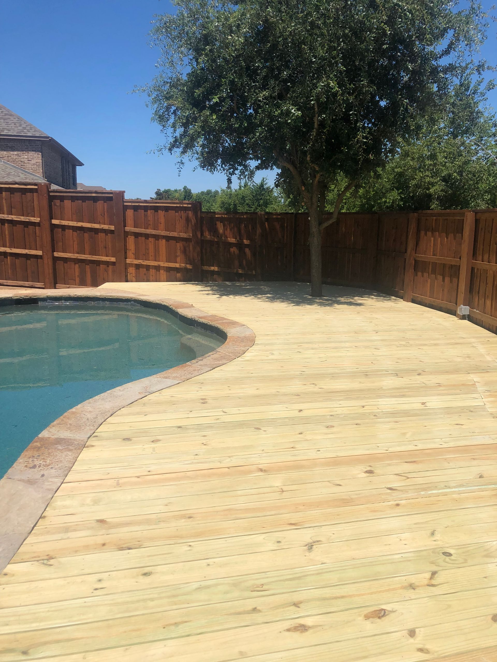 A wooden deck next to a swimming pool with a wooden fence.