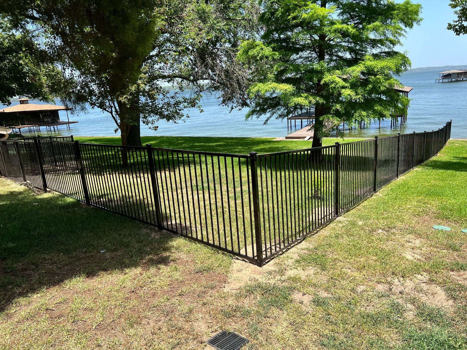 A black fence surrounds a grassy area next to a body of water.