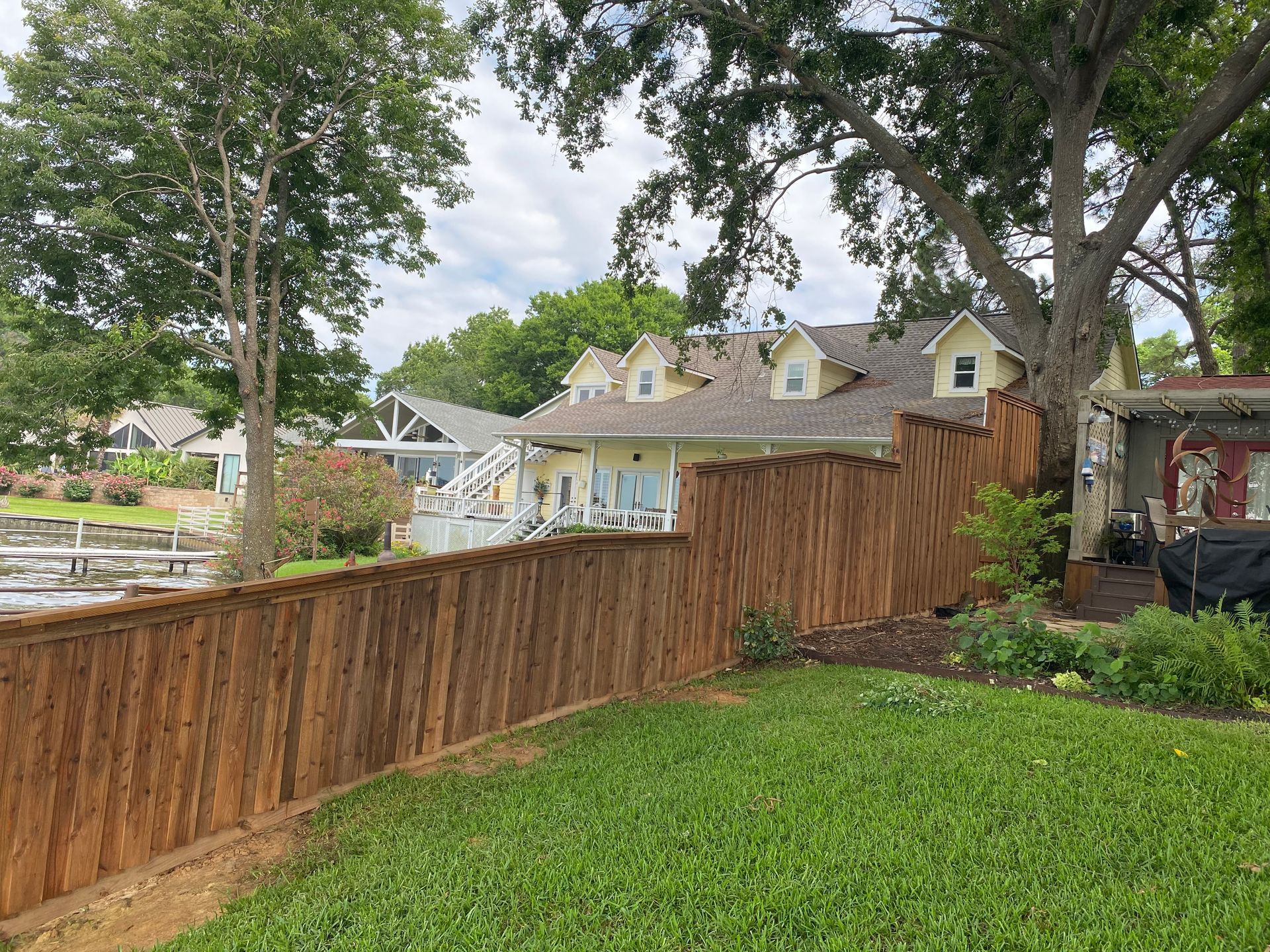 A wooden fence surrounds a lush green yard in front of a house.