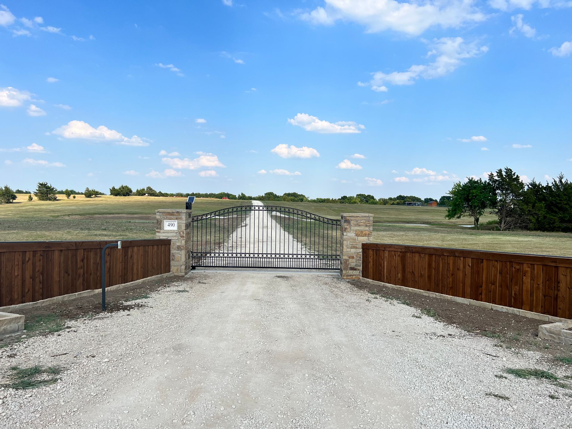 A gravel road with a gate in the middle of it and a wooden fence.