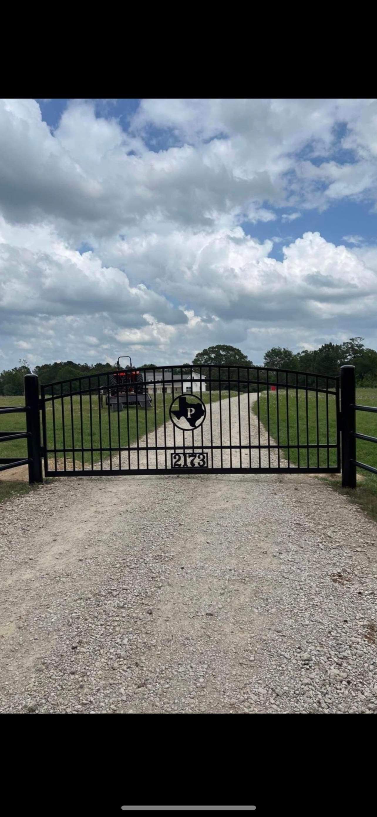 A fence surrounds a gravel road leading to a house.