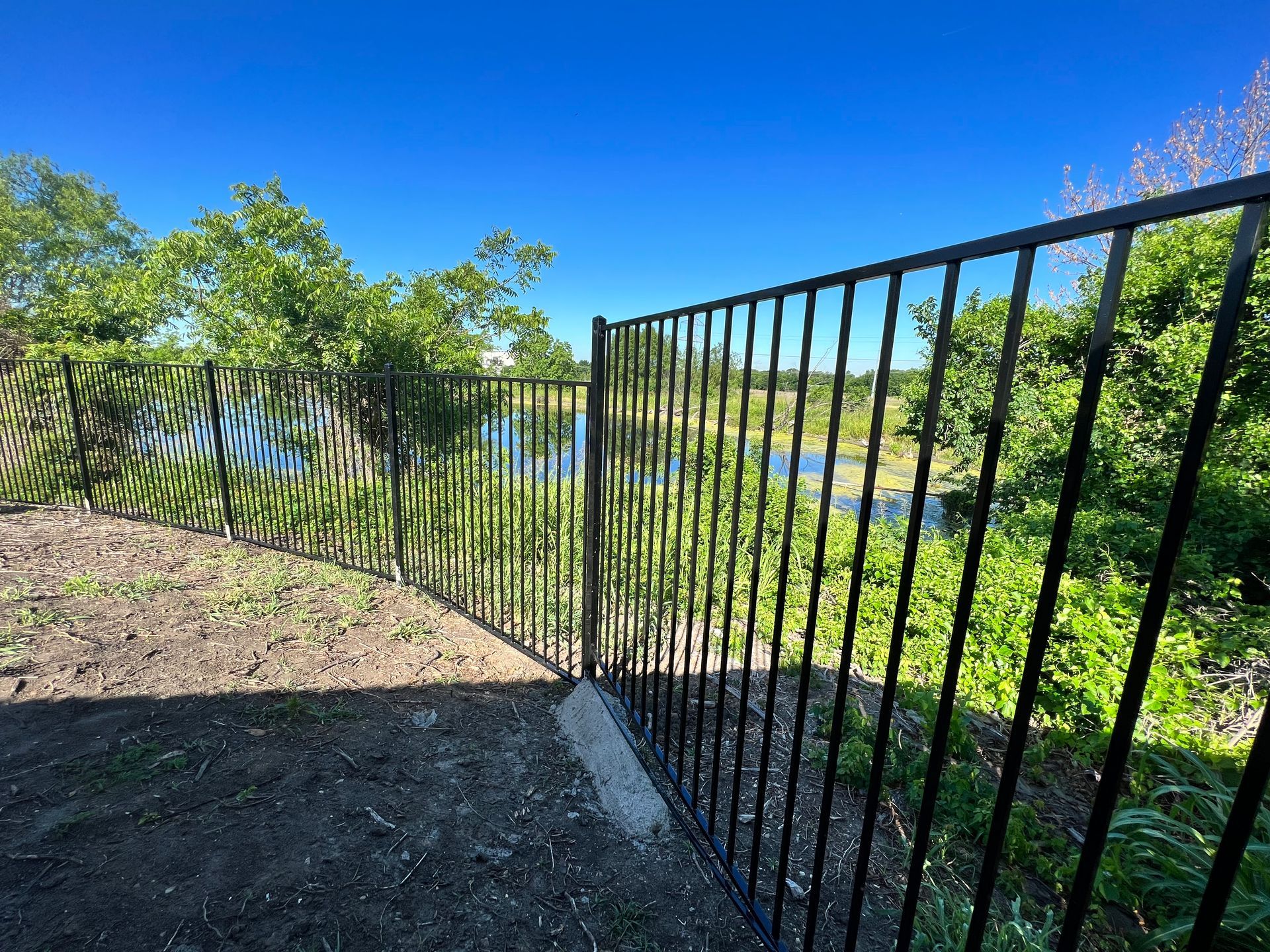 A wrought iron fence surrounds a field with trees and a river in the background.
