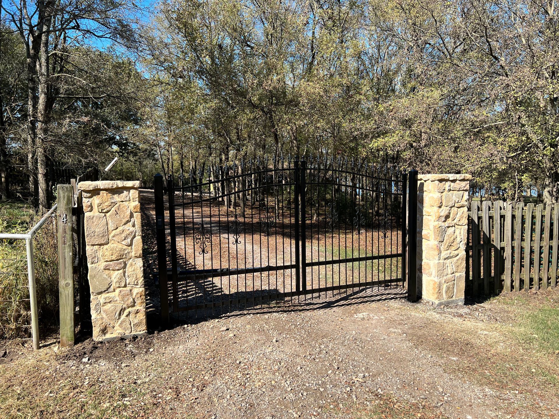 A metal gate is surrounded by stone pillars and a wooden fence.