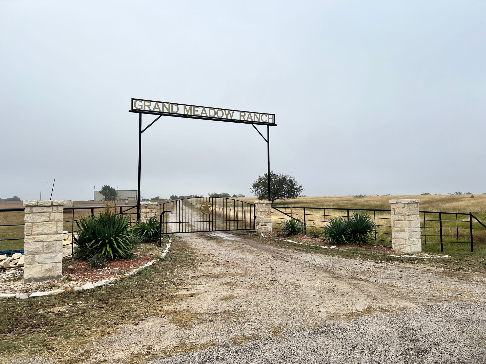 A gravel road leading to a gate with a sign above it.