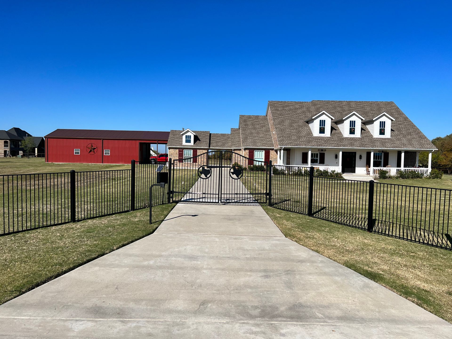 A driveway leading to a large house with a red barn in the background.