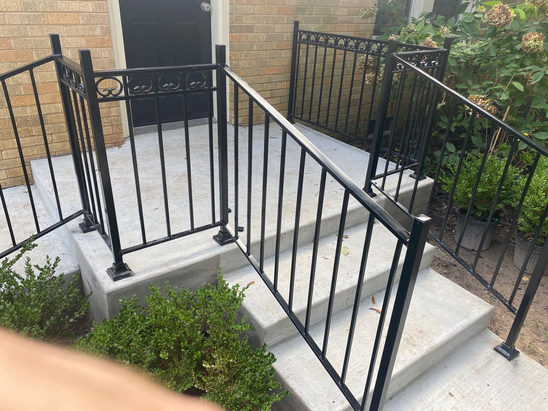 A person is standing in front of a staircase with a wrought iron railing.