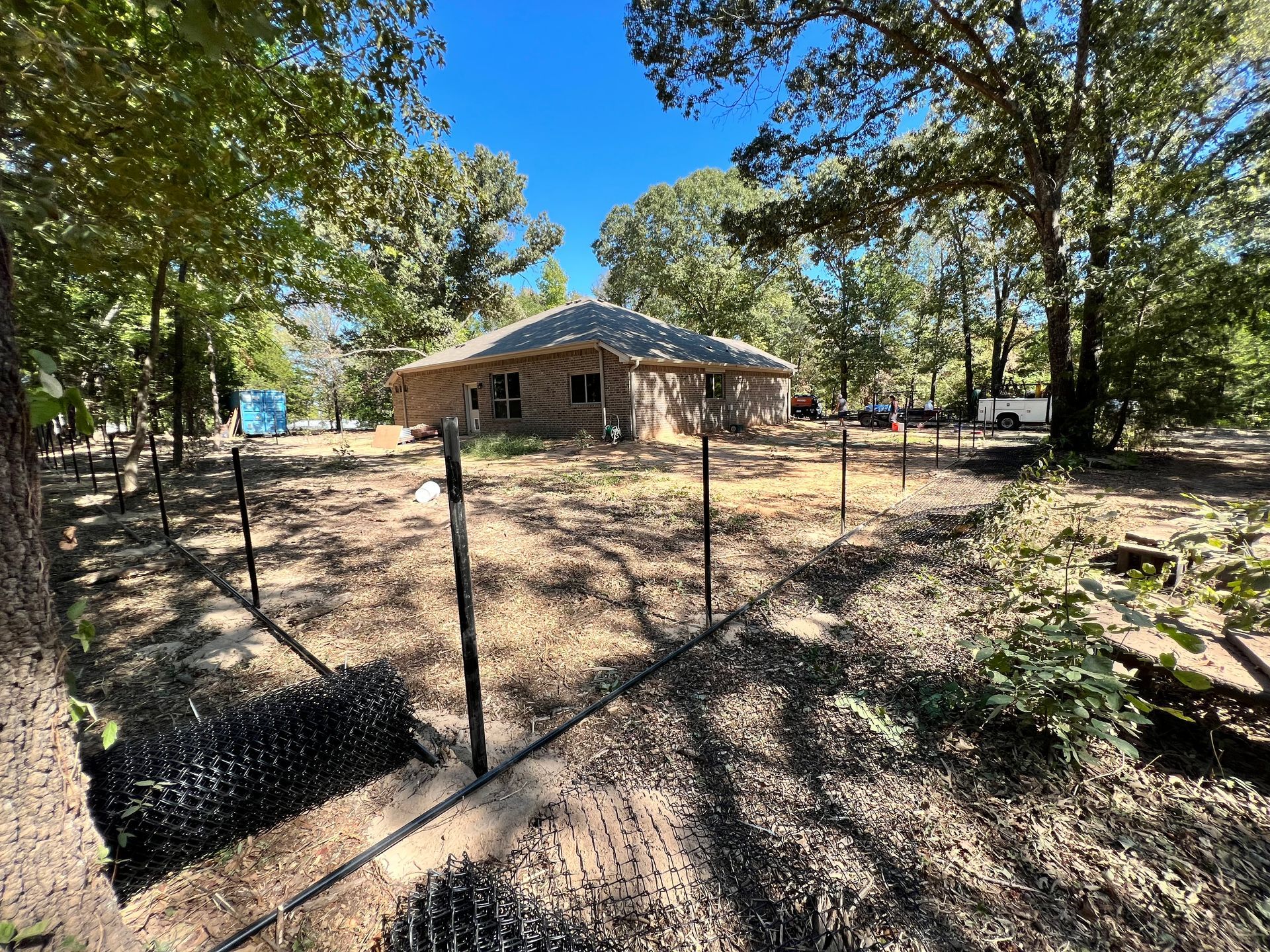 A house is surrounded by trees and a fence in the middle of a field.