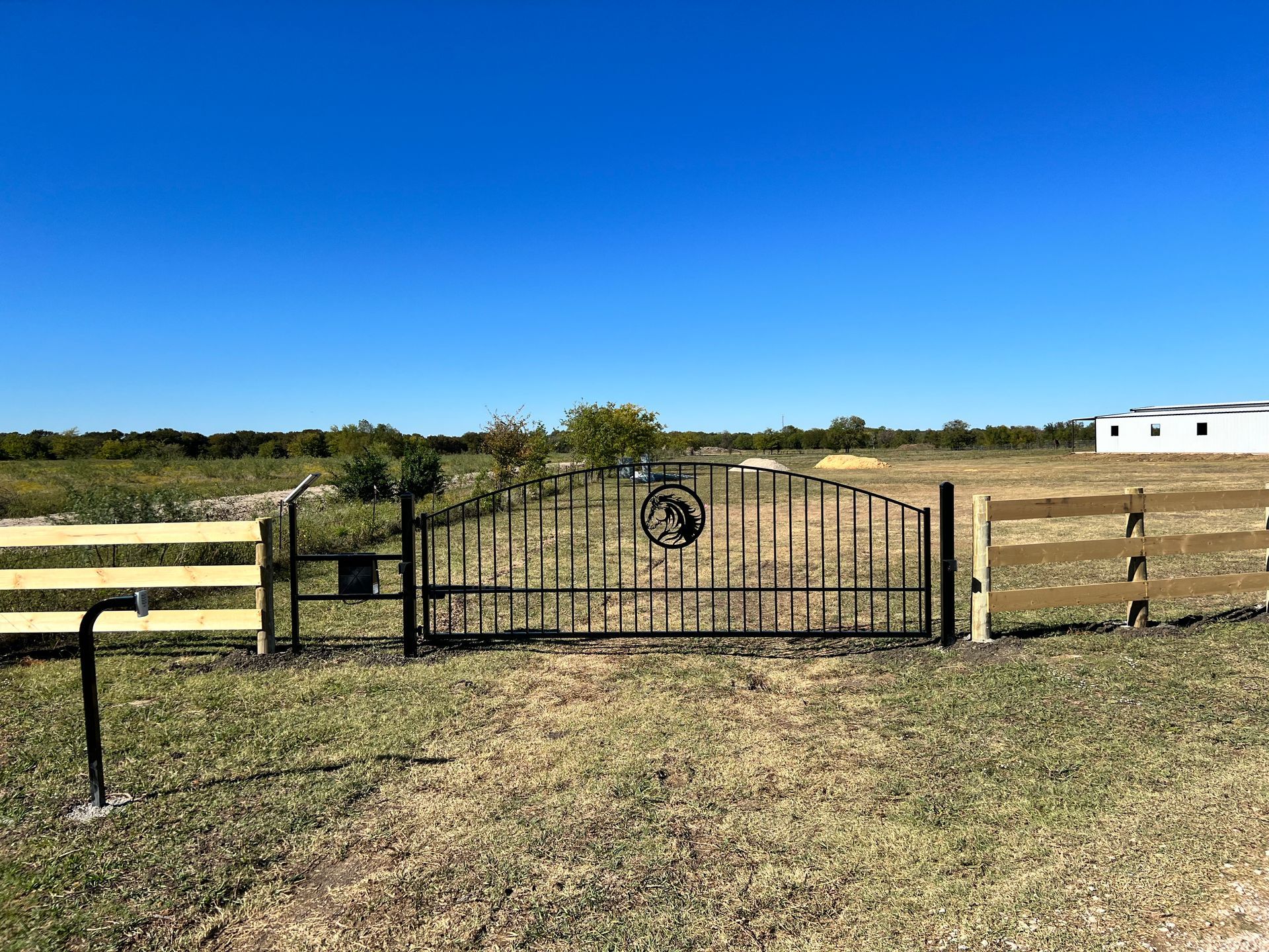 A metal gate is surrounded by a wooden fence in a field.