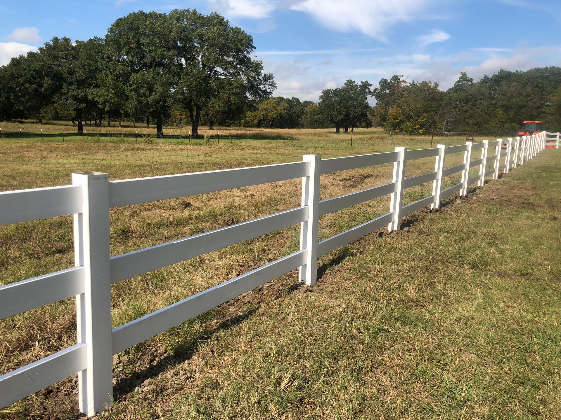 A white fence surrounds a grassy field with trees in the background