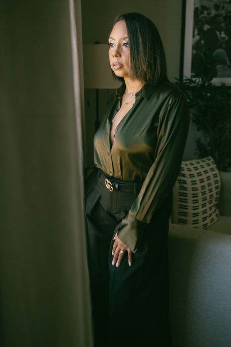 A woman in a green shirt and black pants is standing in front of a window.