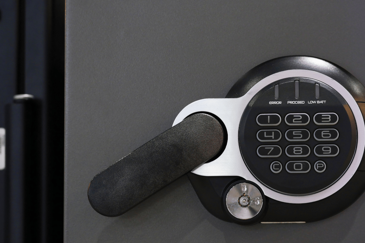 Close-up of a gray safe door with a black digital keypad, handle, and a silver button.