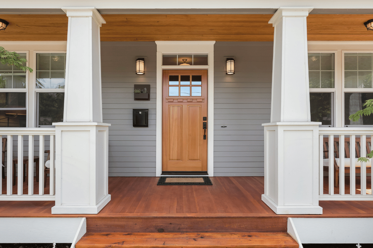Front porch with wooden door, white pillars, and steps.