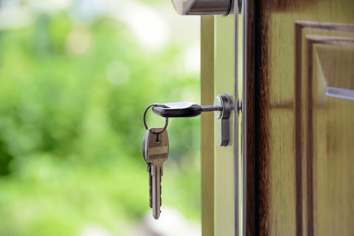 Keys in the lock of a partially open wooden door with a green, blurred background.