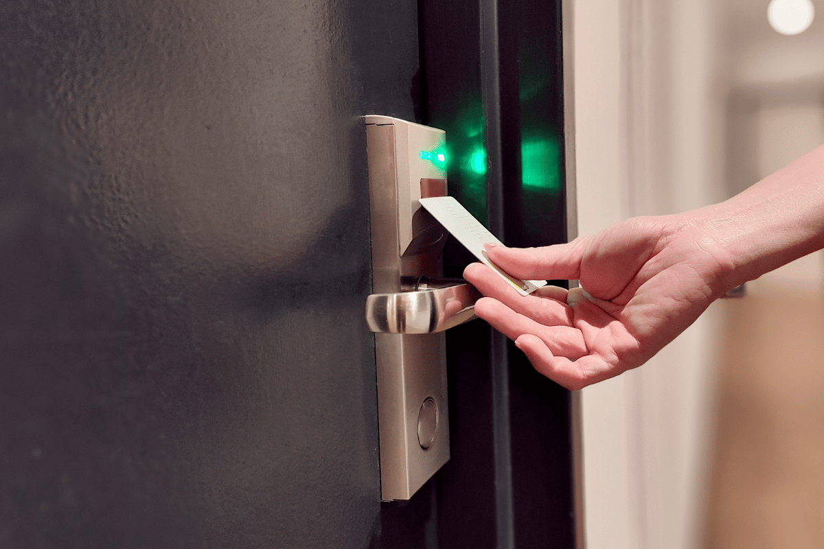 Hand swipes key card on hotel door lock; green lights illuminate.