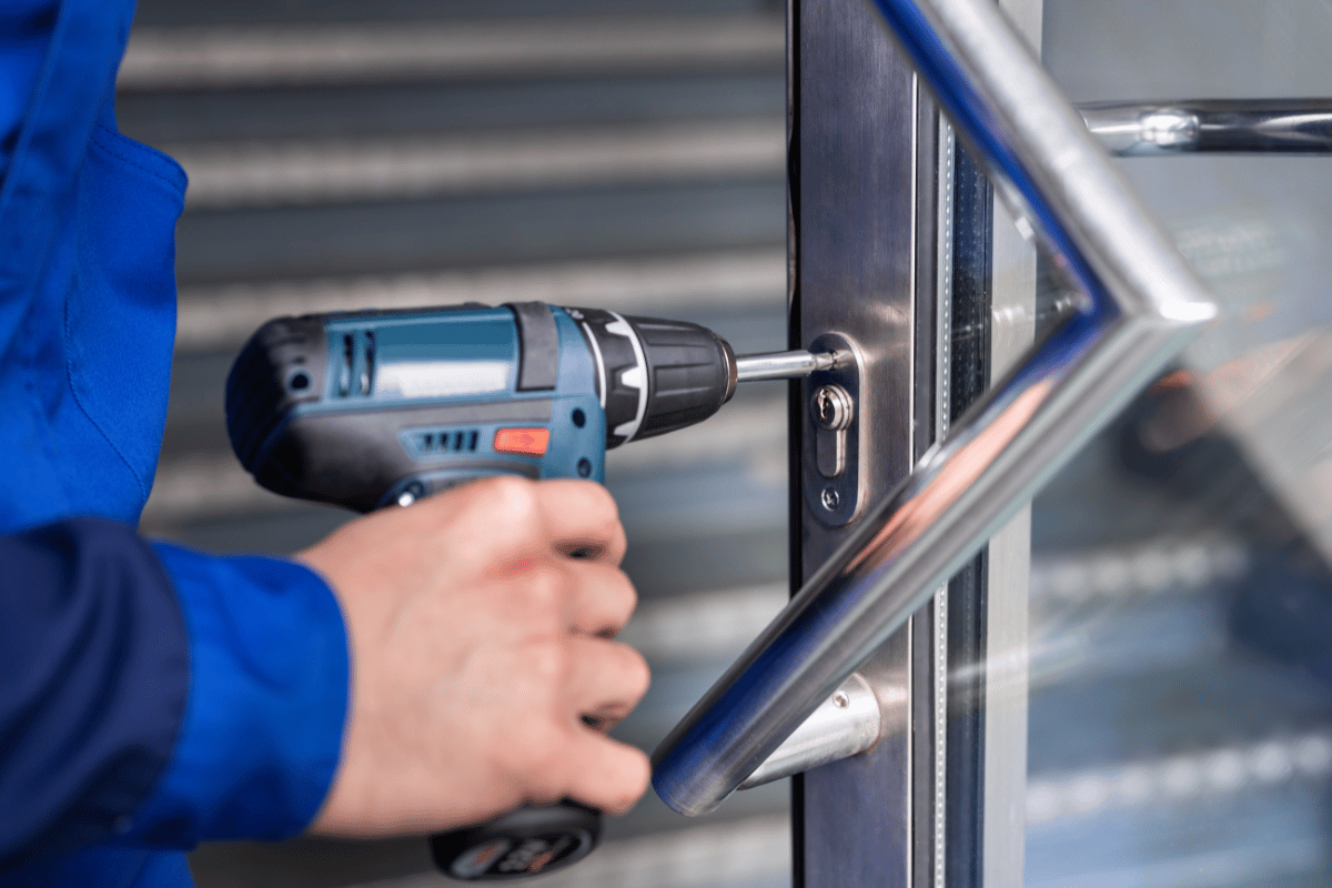Person in blue uniform using a power drill to install a metal door handle.