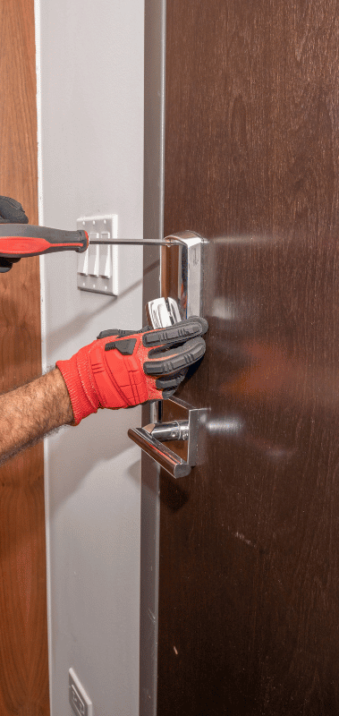 Person in red gloves using a screwdriver to install a door lock.