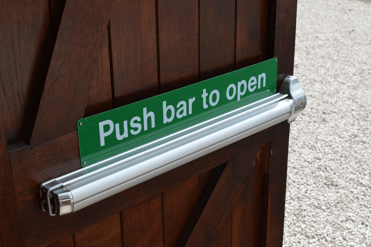 Wooden door with a silver push bar and a green sign reading 