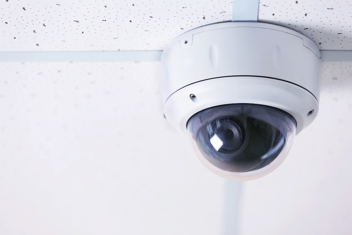 Security camera mounted on a white ceiling with grid lines.