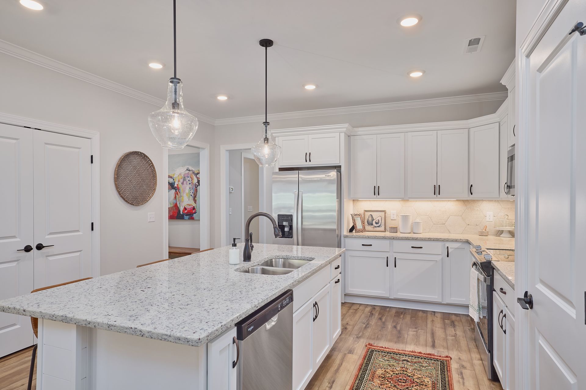 Bright white kitchen with granite island, stainless steel appliances, and wood flooring.
