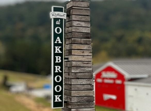 Sign for "Retreat at Oakbrook" beside a wooden post with a red barn in the background.