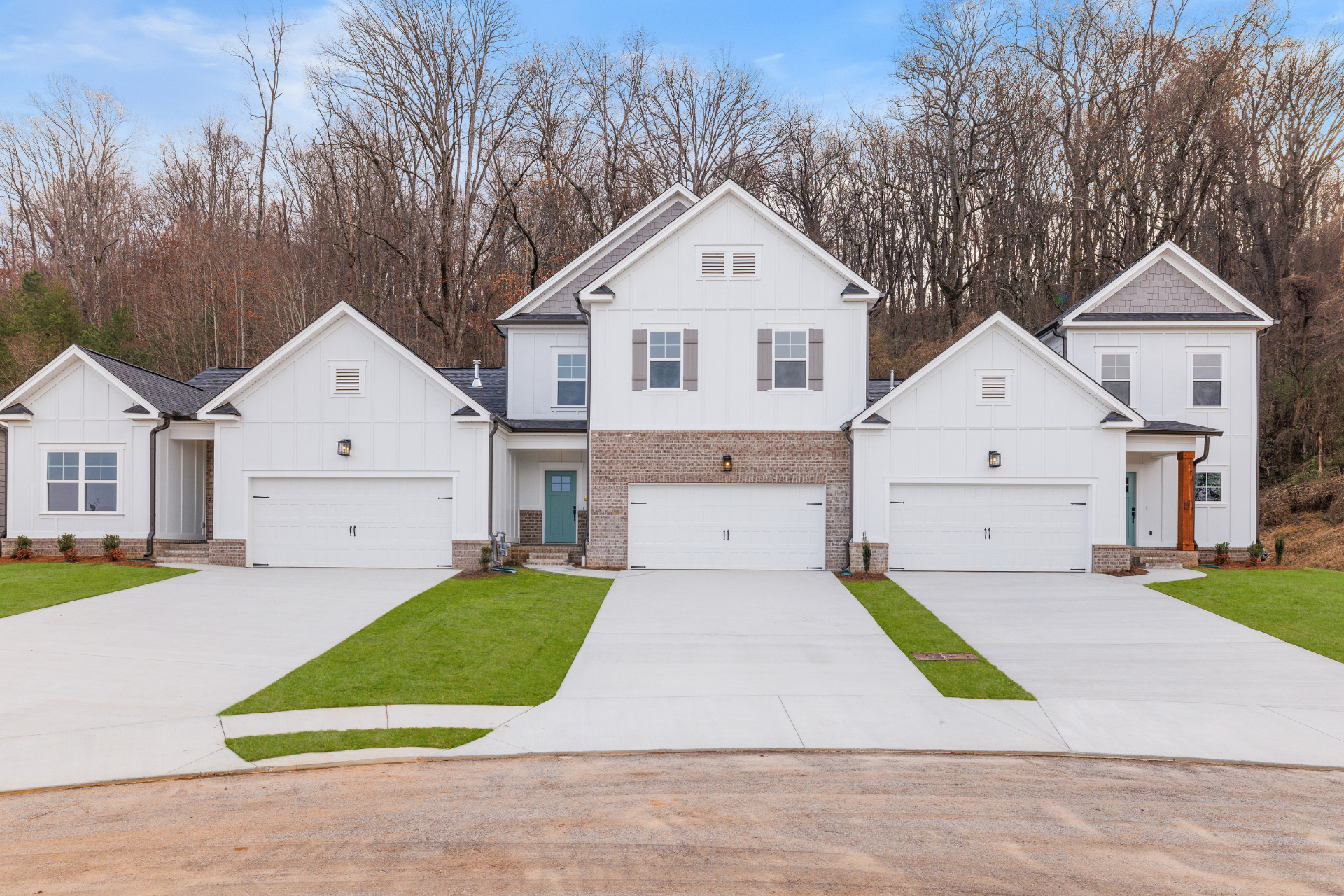 White houses with attached garages and driveways, set against a backdrop of trees.