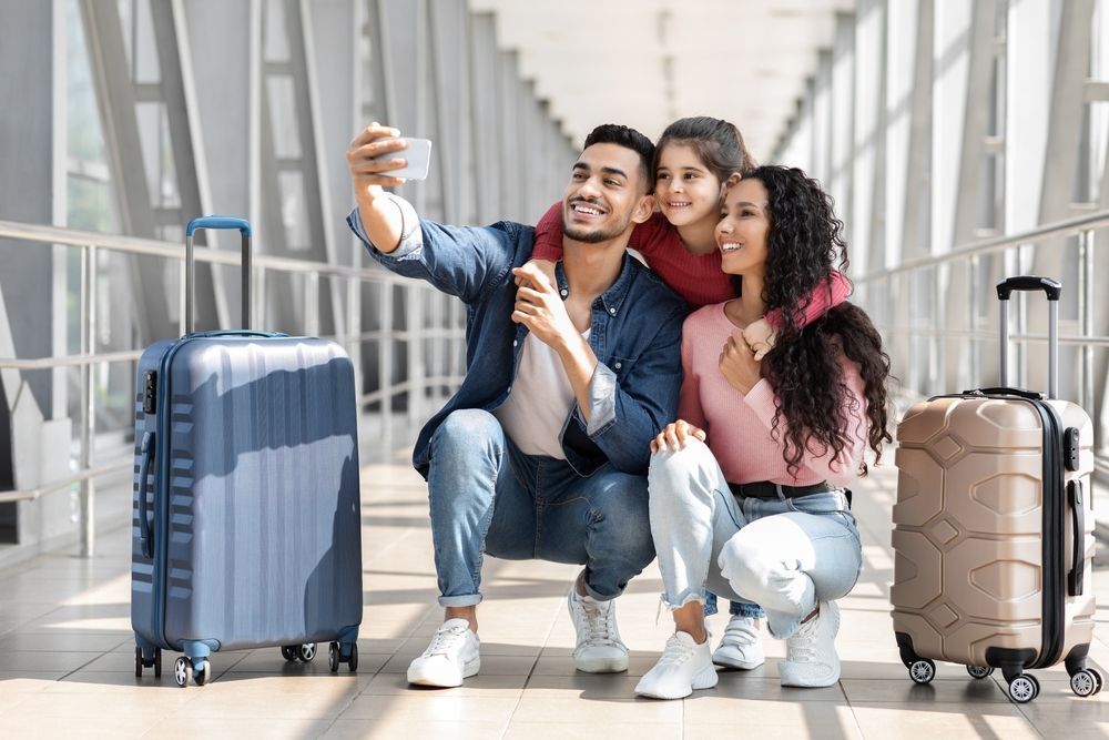 A family is taking a selfie at the airport with their luggage.