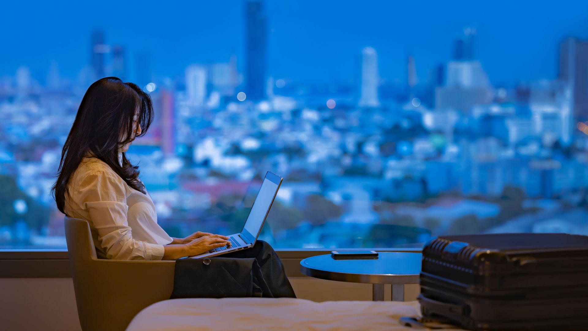 A woman is sitting in front of a window using a laptop computer.