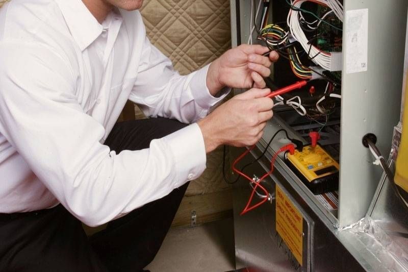 A person in a white shirt tests electrical wiring inside a metal appliance with a multimeter.