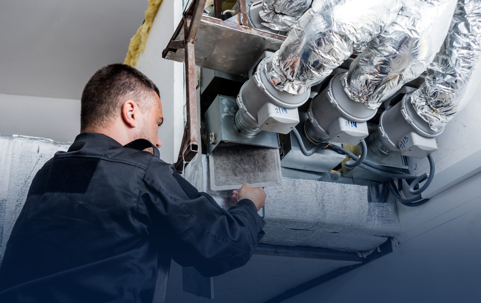 HVAC technician working on an air duct system with insulated pipes, indoors.
