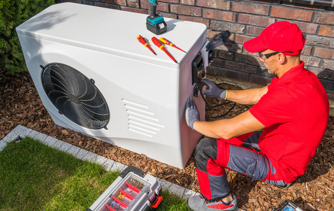 Person in red work clothes installing an outdoor unit near a brick wall, tools nearby.
