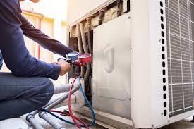 Person servicing an AC unit, using gauges. White and metal equipment in outdoor setting.