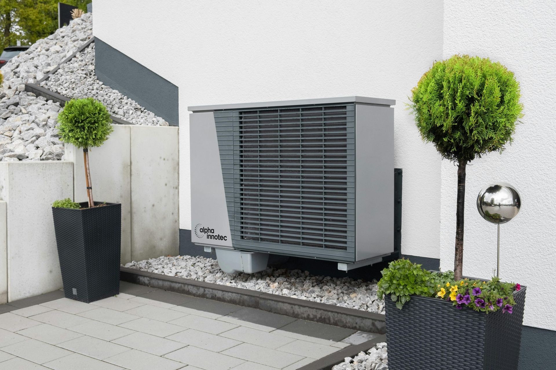 Modern outdoor HVAC unit beside a white building, framed by potted plants and gravel landscaping