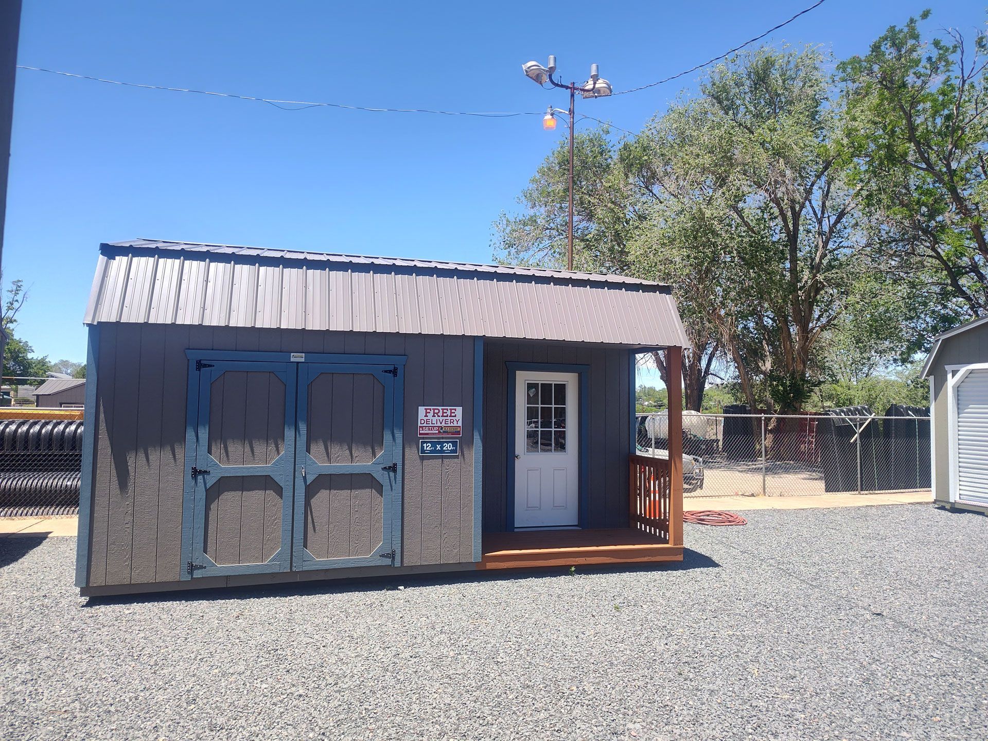 Small gray shed with blue double doors and white side door on a gravel lot under a clear sky.